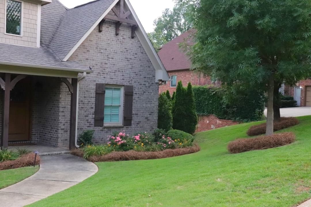 Charming brick home with green window shutters, landscaped garden, and curved pathway.