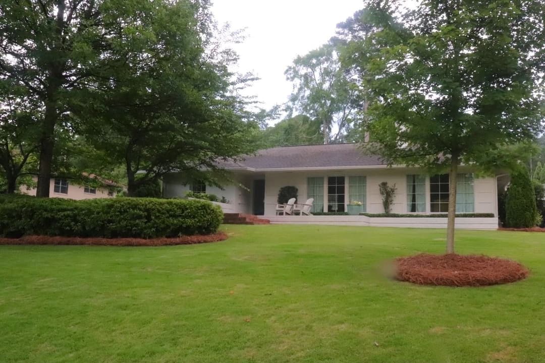 Charming single-story home with green lawn, shrubs, and peaceful front porch seating.