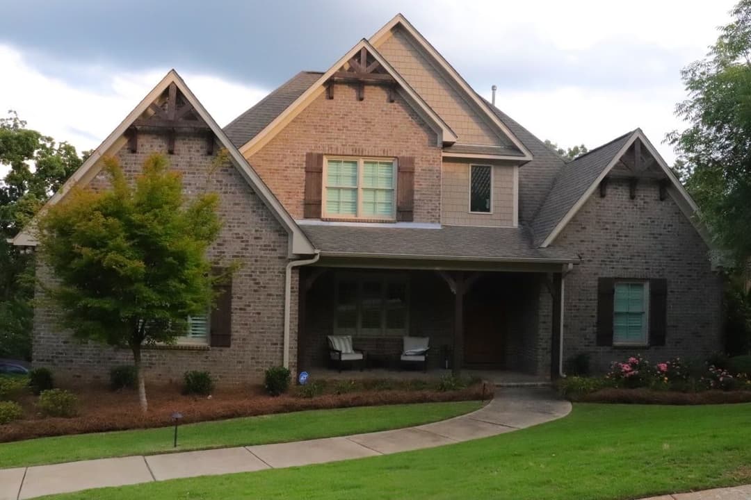 Elegant brick house with gabled roof, lush landscaping, and inviting front porch.
