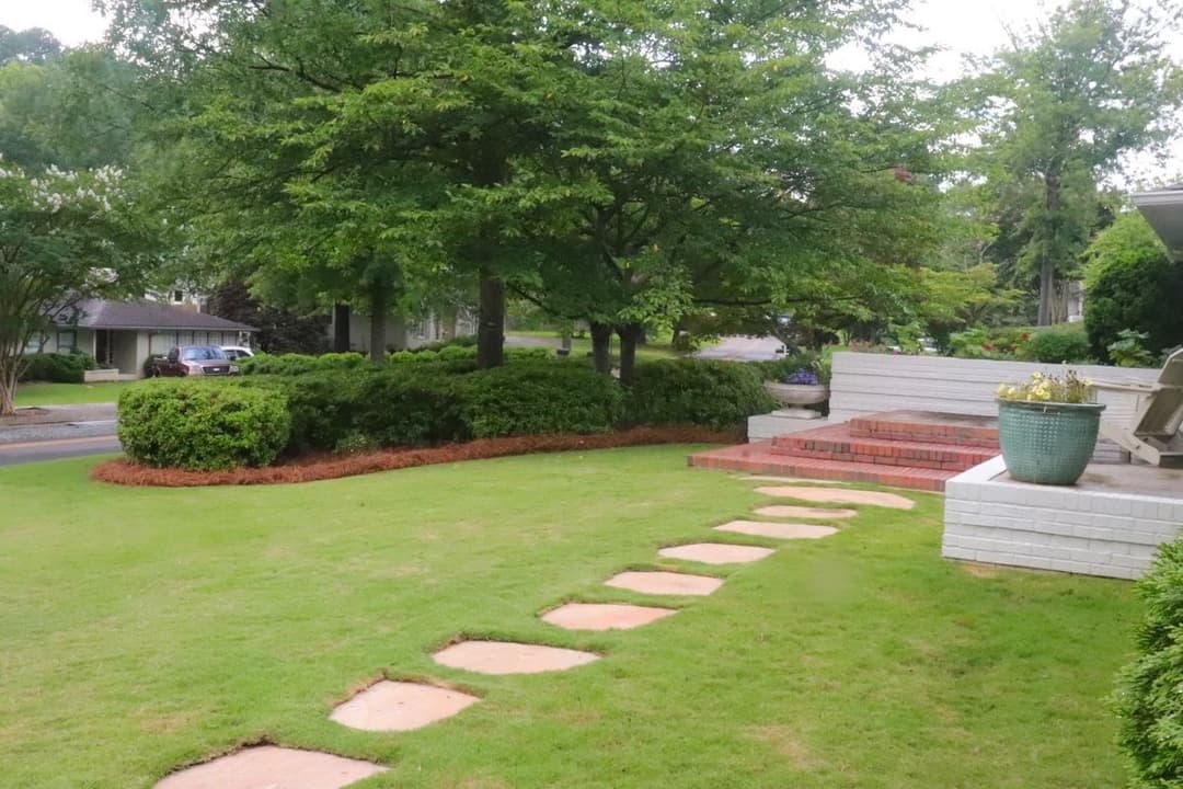 Lush green lawn with stone pathway, bordered by shrubs and a modern patio area.
